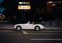 A white sports car driving down a street at night